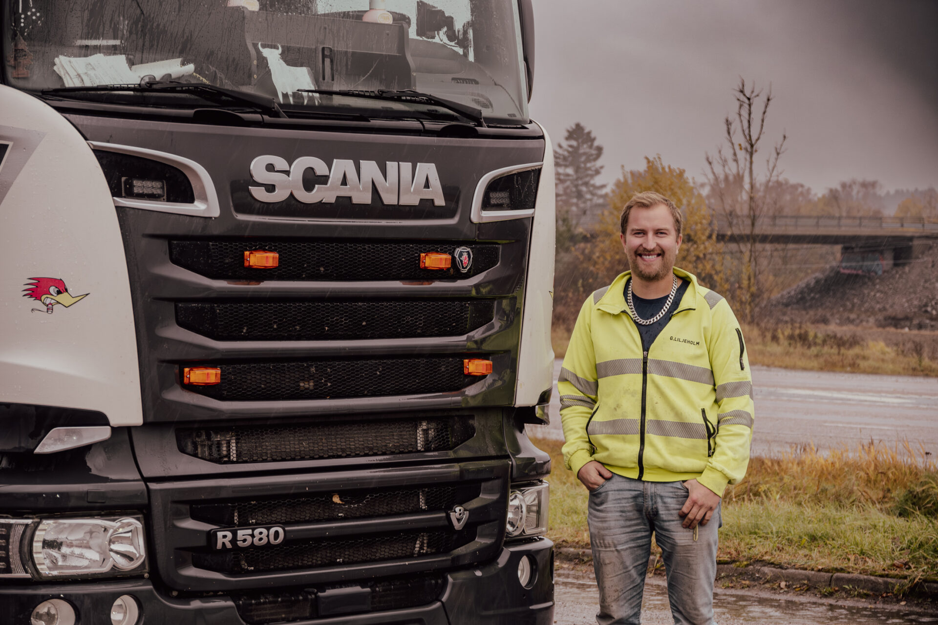 Upptäck en unik glimt av Gurra Liljeholm, den karismatiska lastbilsföraren, som stolt står bredvid sin glänsande Scania. En bild som fångar essensen av väglivet och den oförutsägbara charmen hos oväntade möten.